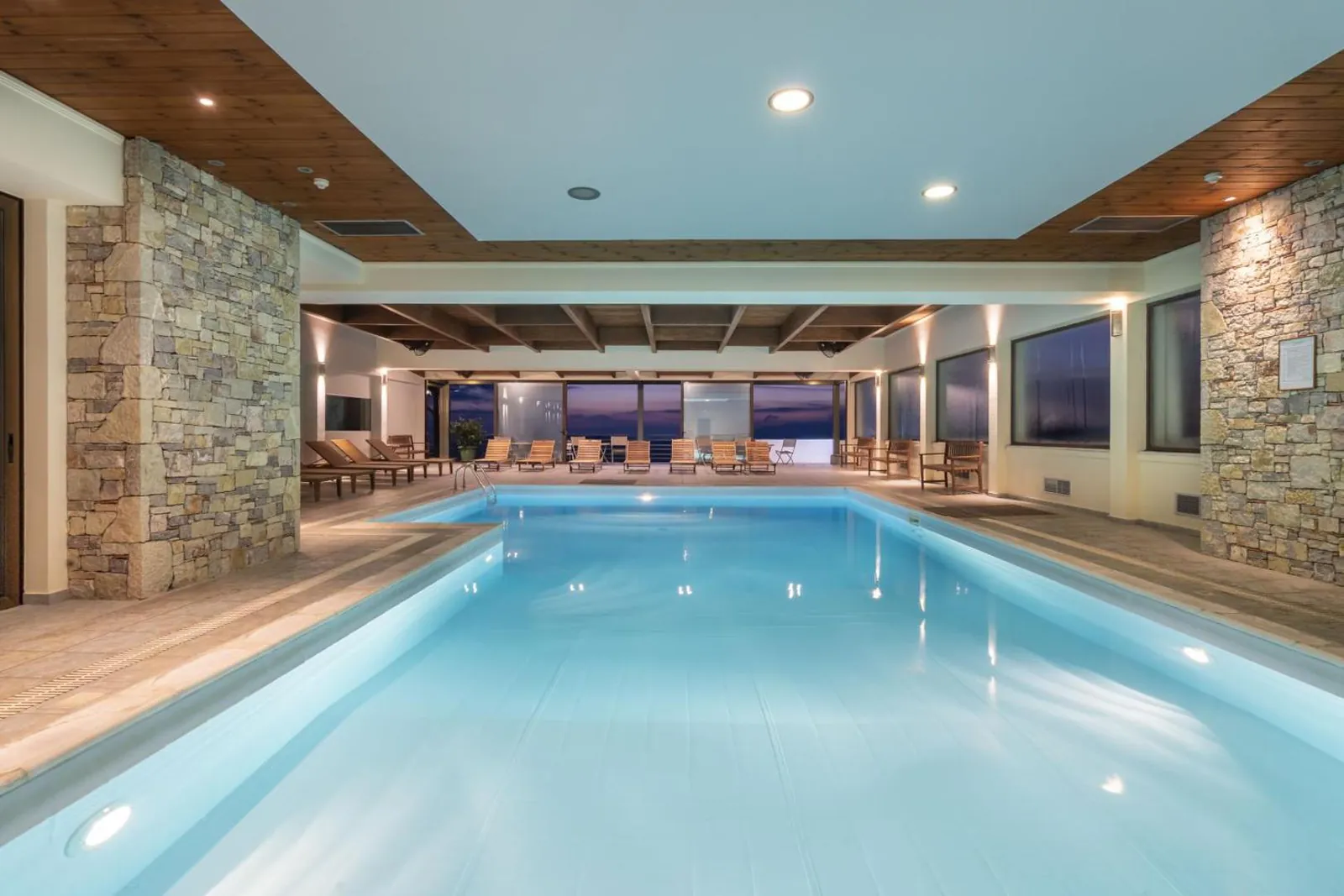 Indoor pool with stone walls and a row of loungers facing the windows at Anemolia Mountain Resort