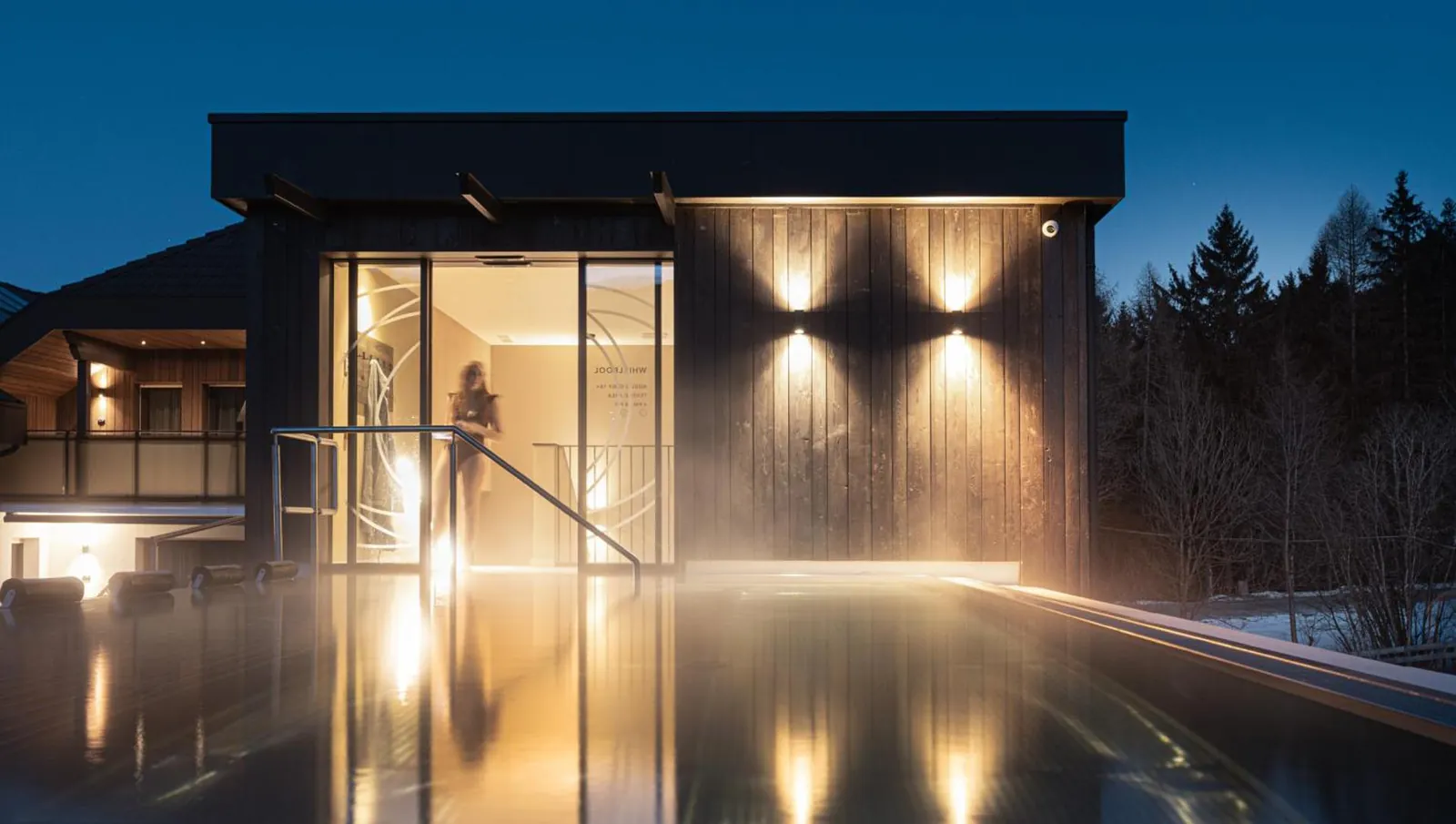 Outdoor pool glowing at dusk beside the spa building