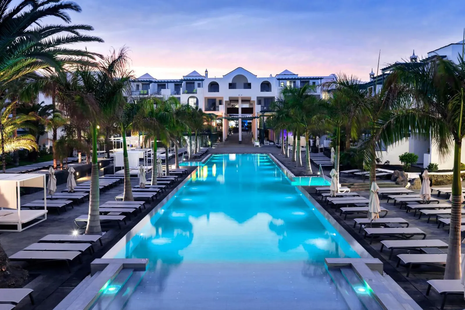 Outdoor pool at dusk at Barceló Teguise Beach, hotel wings lit on both sides