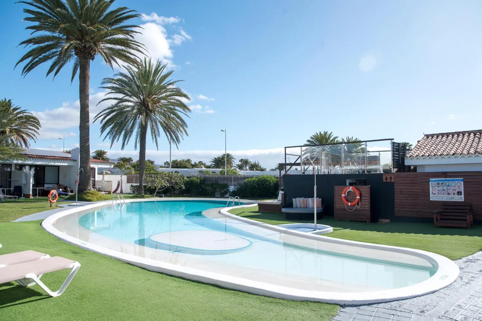 Curving pool on a lawn of palms and loungers at Bungalows El Palmital