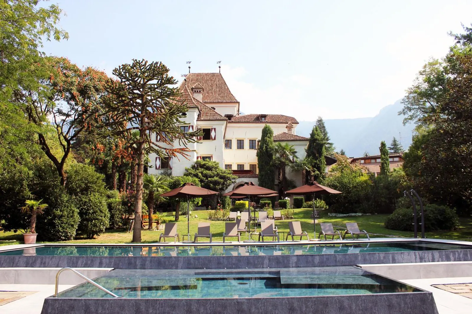 Outdoor pool in the garden at Castel Rundegg, with the castle and mountains behind