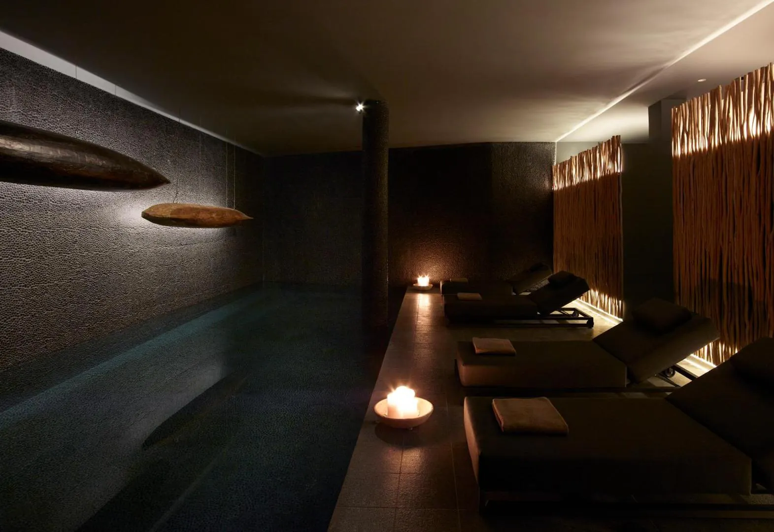 Indoor spa pool lit by candles, with loungers alongside