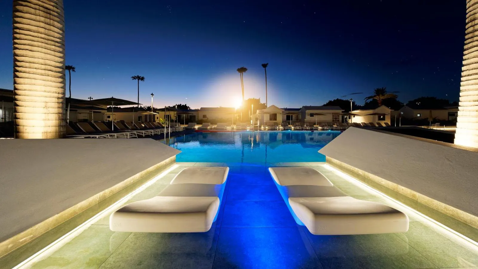 Sun loungers set in the pool water, lit up at night