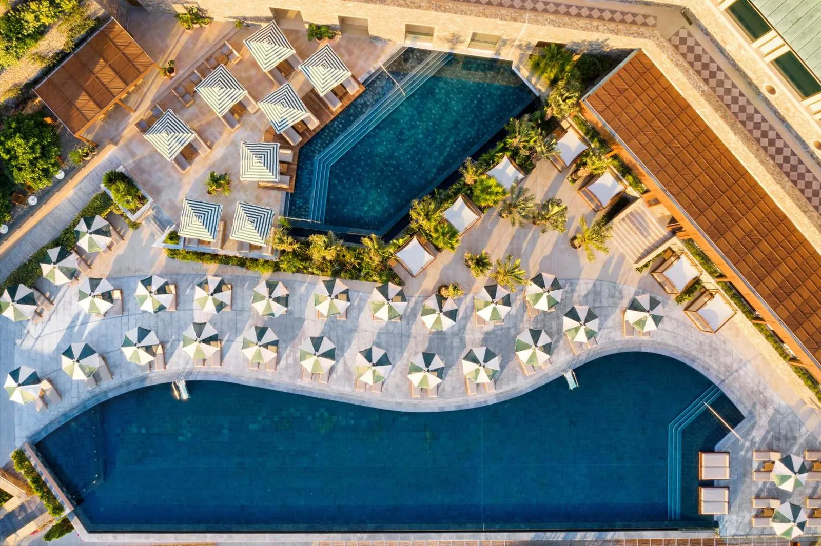 Two pools curving through rows of striped umbrellas, seen from above