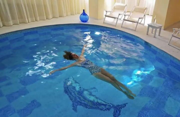 Round-edged indoor pool with a mosaic floor and white loungers