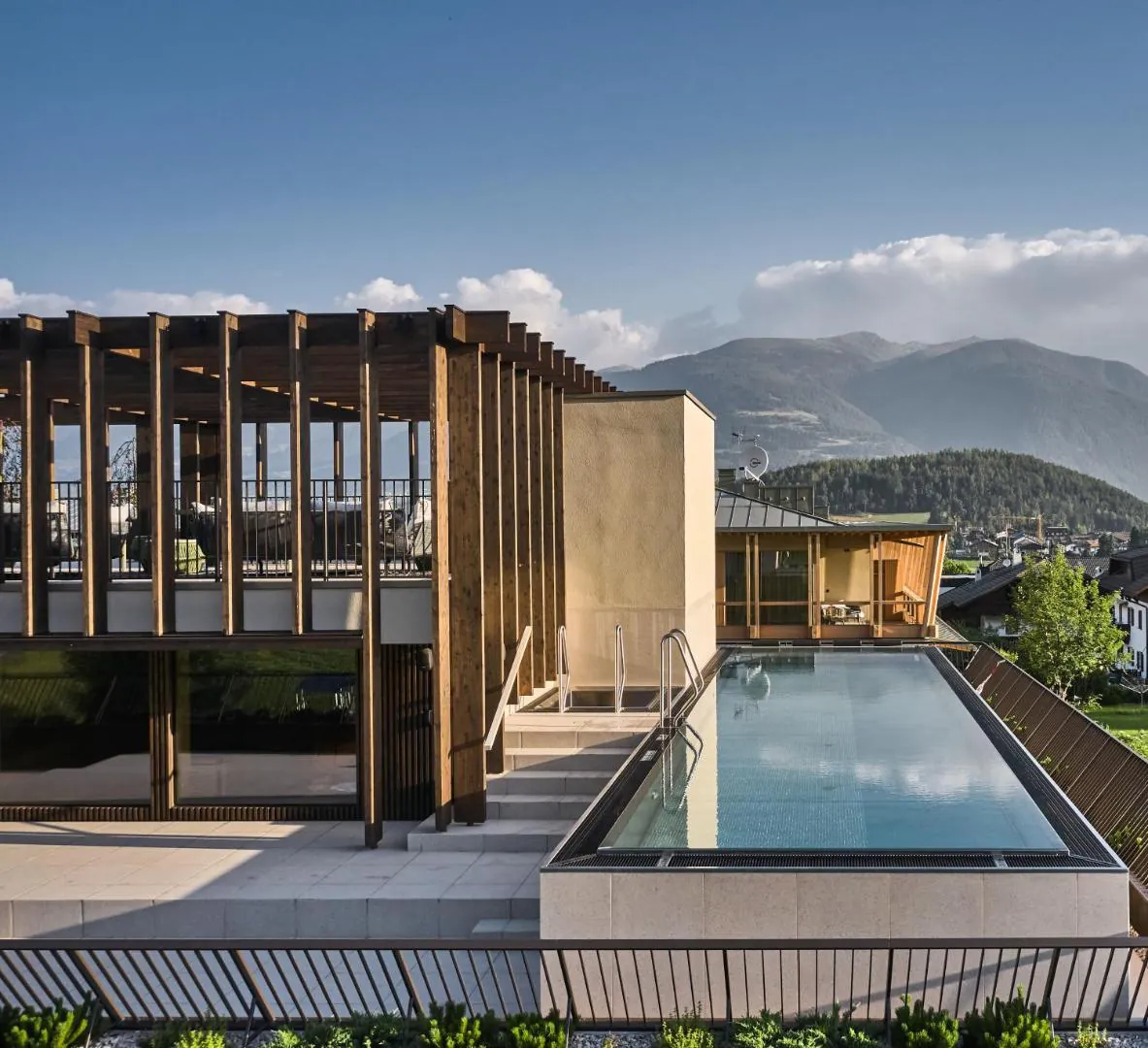 Rooftop infinity pool at Falkensteiner Hotel Kronplatz, with the timber pergola and the Puster valley mountains behind