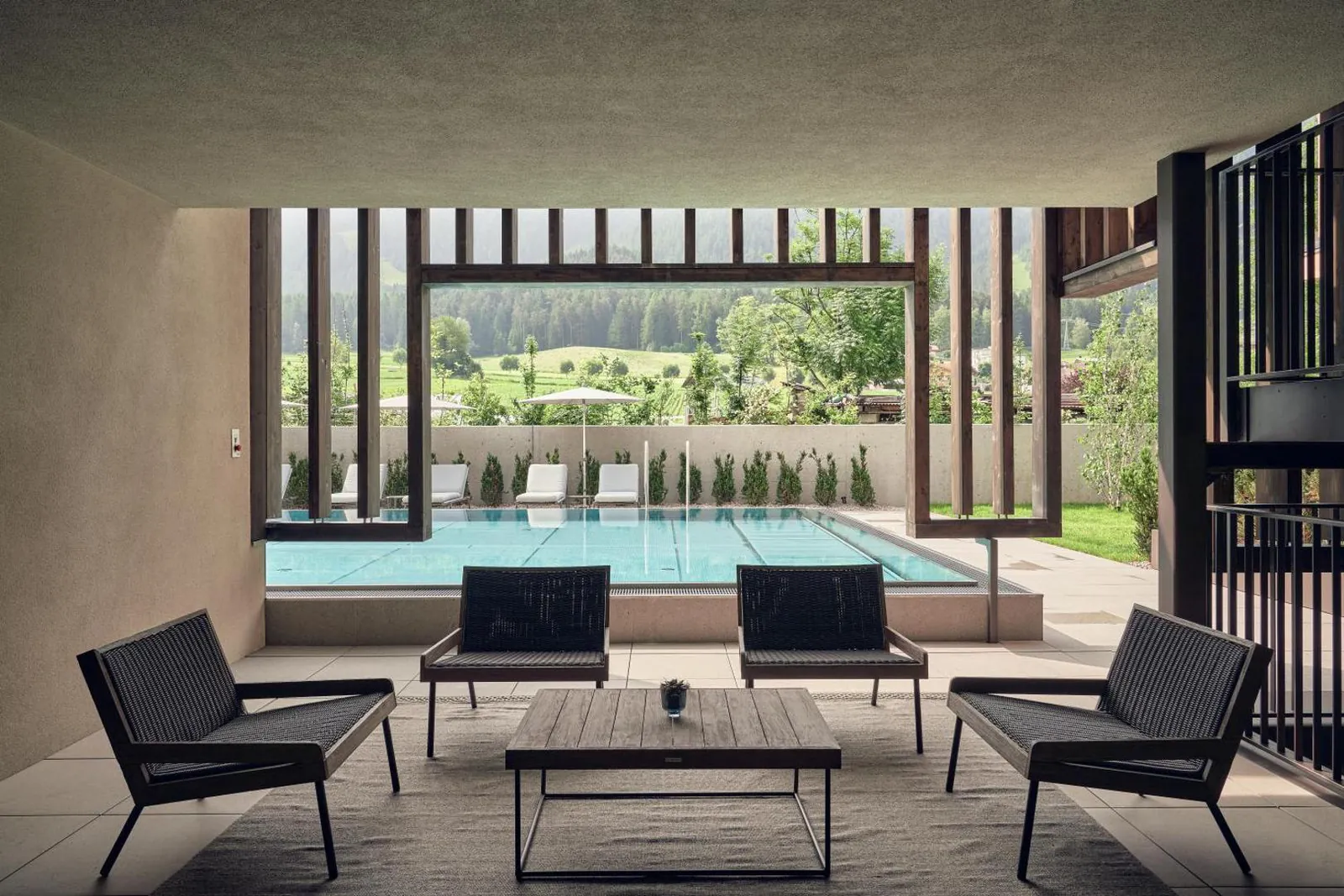Lounge chairs inside the spa, looking out through tall frames onto the outdoor pool
