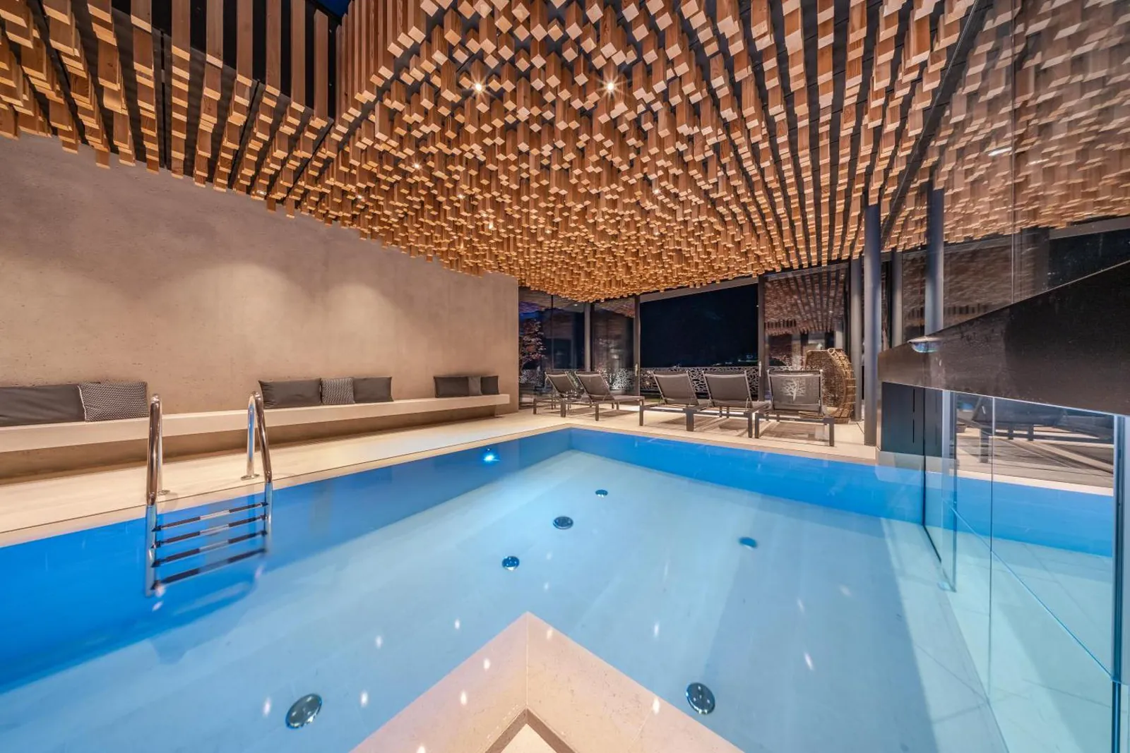 Heated pool running from inside under a slatted wooden ceiling out through a glass partition