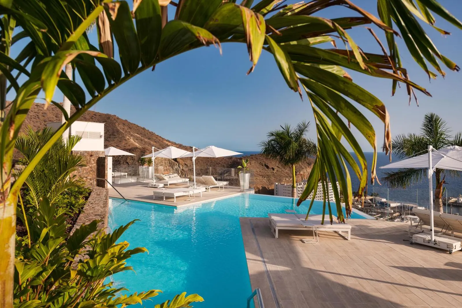 Loungers and parasols around the pool, hills and the marina beyond