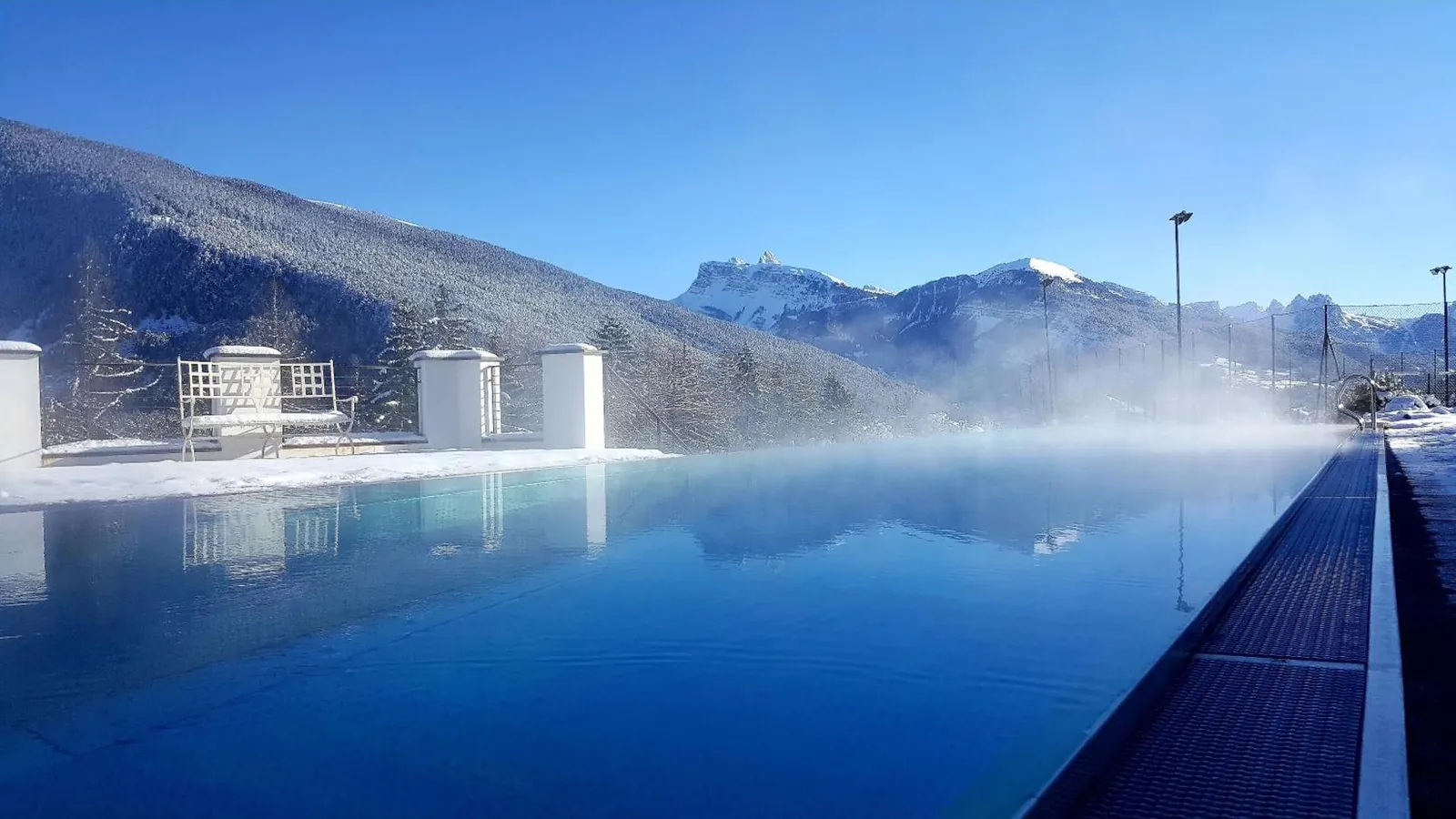 Steam rising off the heated infinity pool on a winter day, snowy peaks across the valley