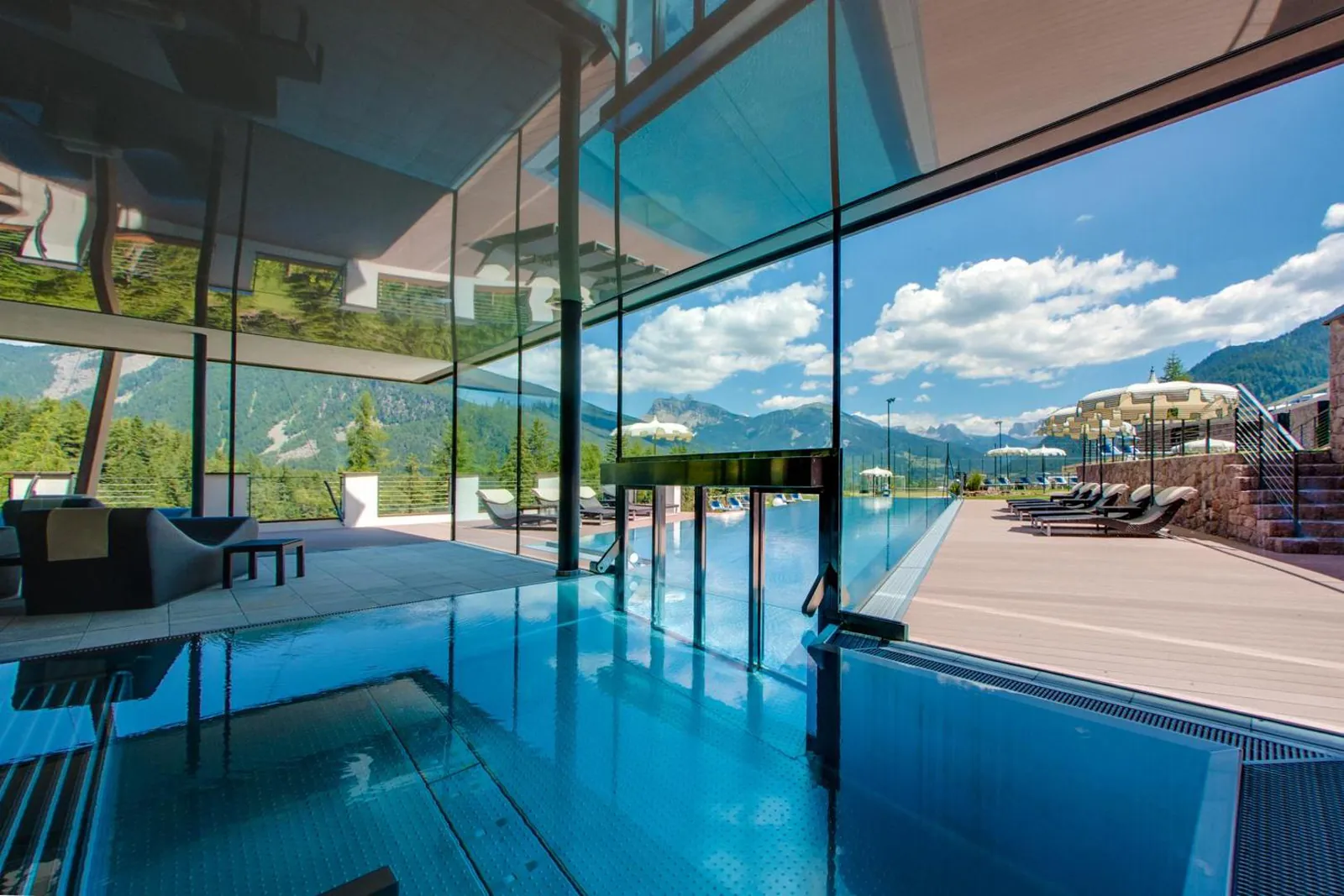 Indoor pool behind glass walls that look out to the outdoor pool and the mountains