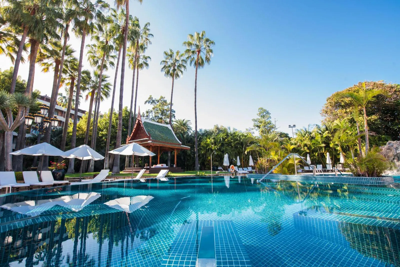 Outdoor pool with loungers and a pagoda among tall palms