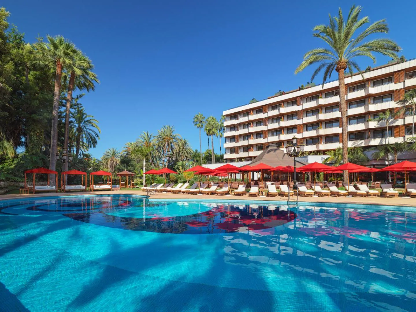 Pool with red parasols below the hotel building