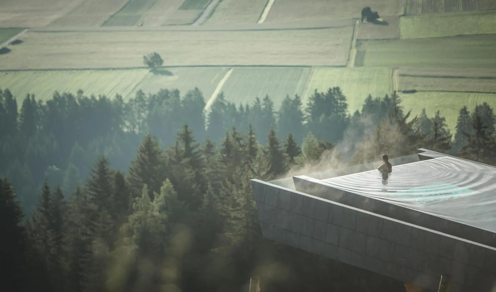 Steam rising off the heated Sky Pool above the forest on a misty morning