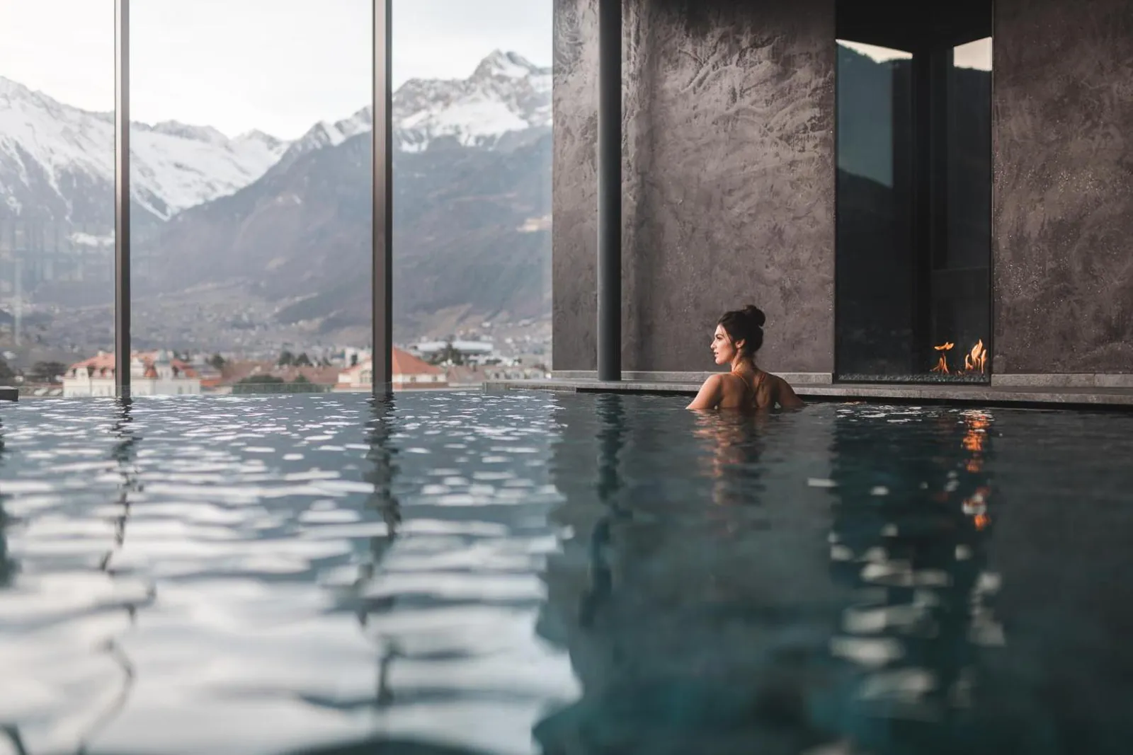 Swimmer at the glass edge of the rooftop pool facing snow-capped peaks