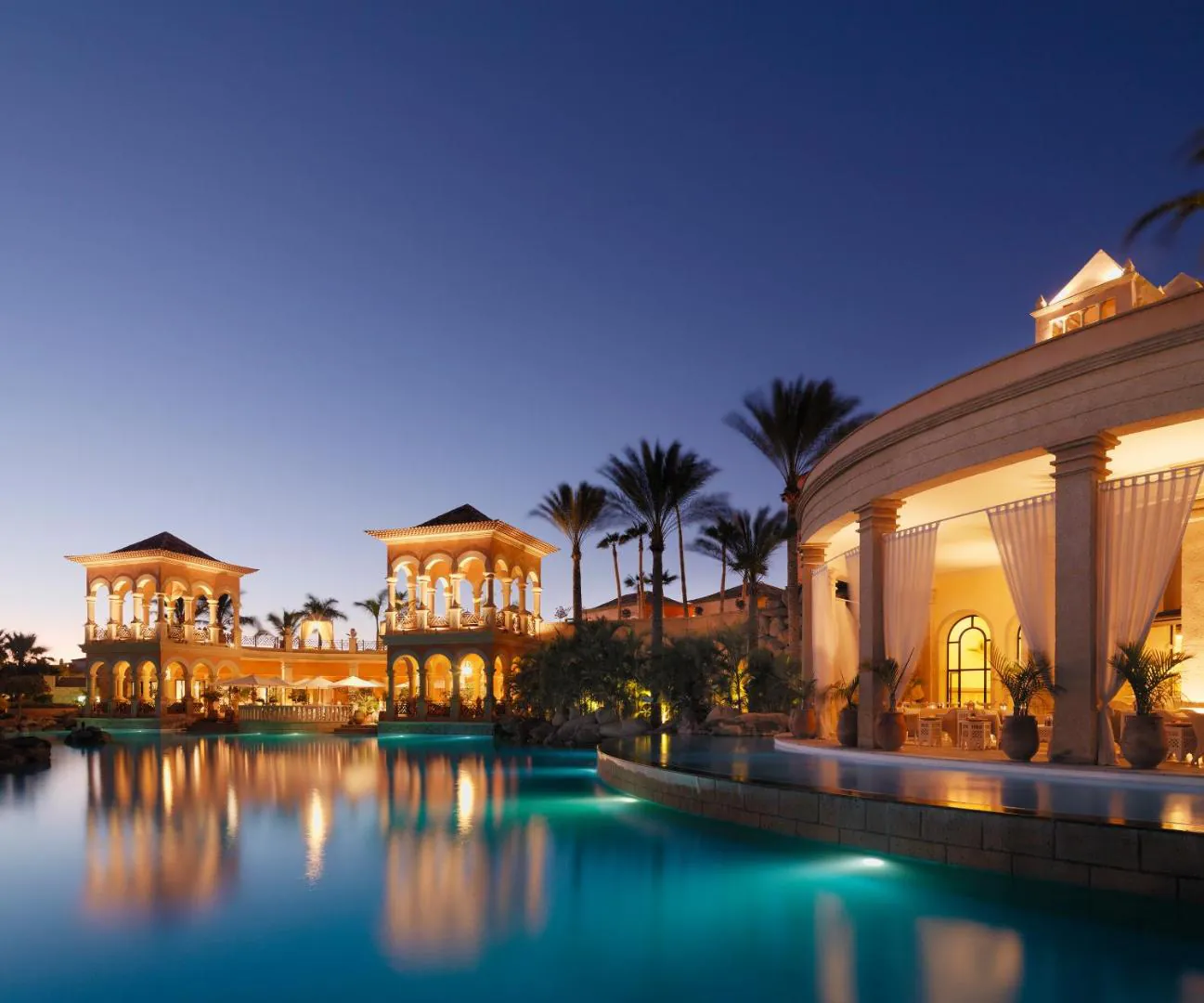 The outdoor pool at JOIA El Mirador lit up at dusk, with the main building behind