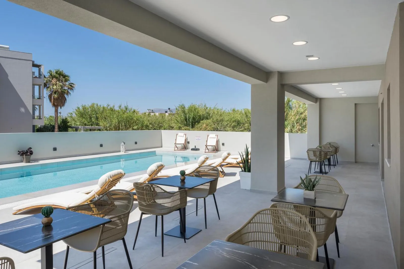 Covered terrace with tables and rattan chairs facing the pool