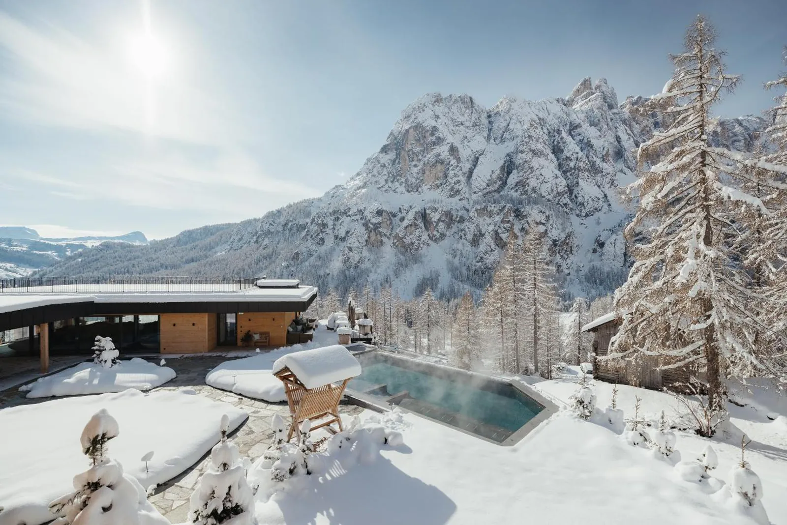 Outdoor pool with snow on the loungers and Dolomite peaks behind
