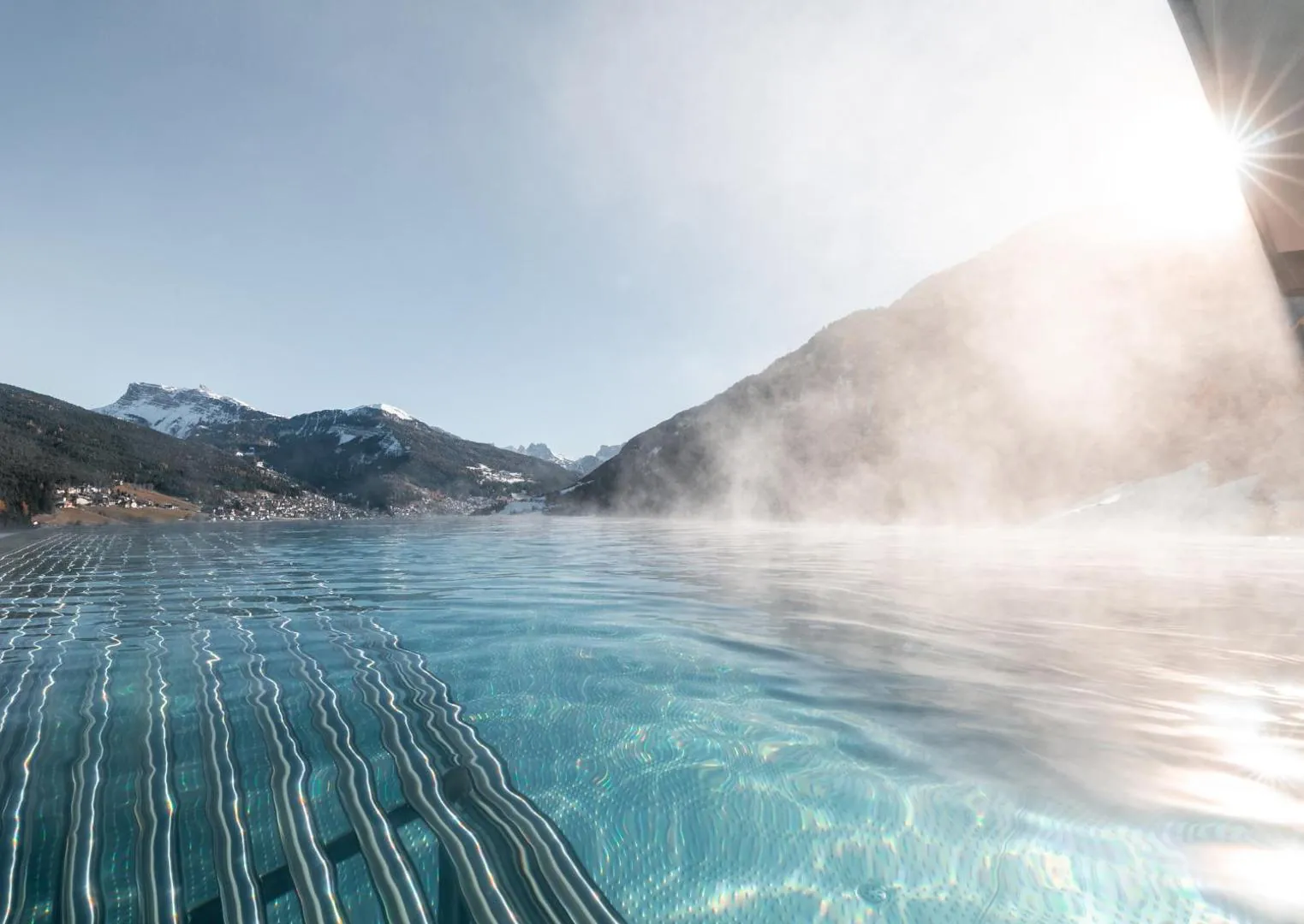 Steam rising from the outdoor pool toward sunlit peaks