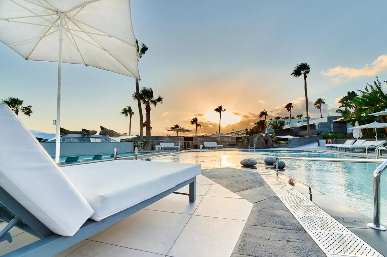 Lounger and parasol beside the pool at sunset, palms along the terrace