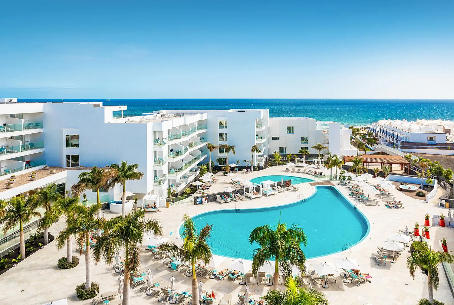 Lagoon-shaped pool among palms with the hotel's white wings and the Atlantic behind