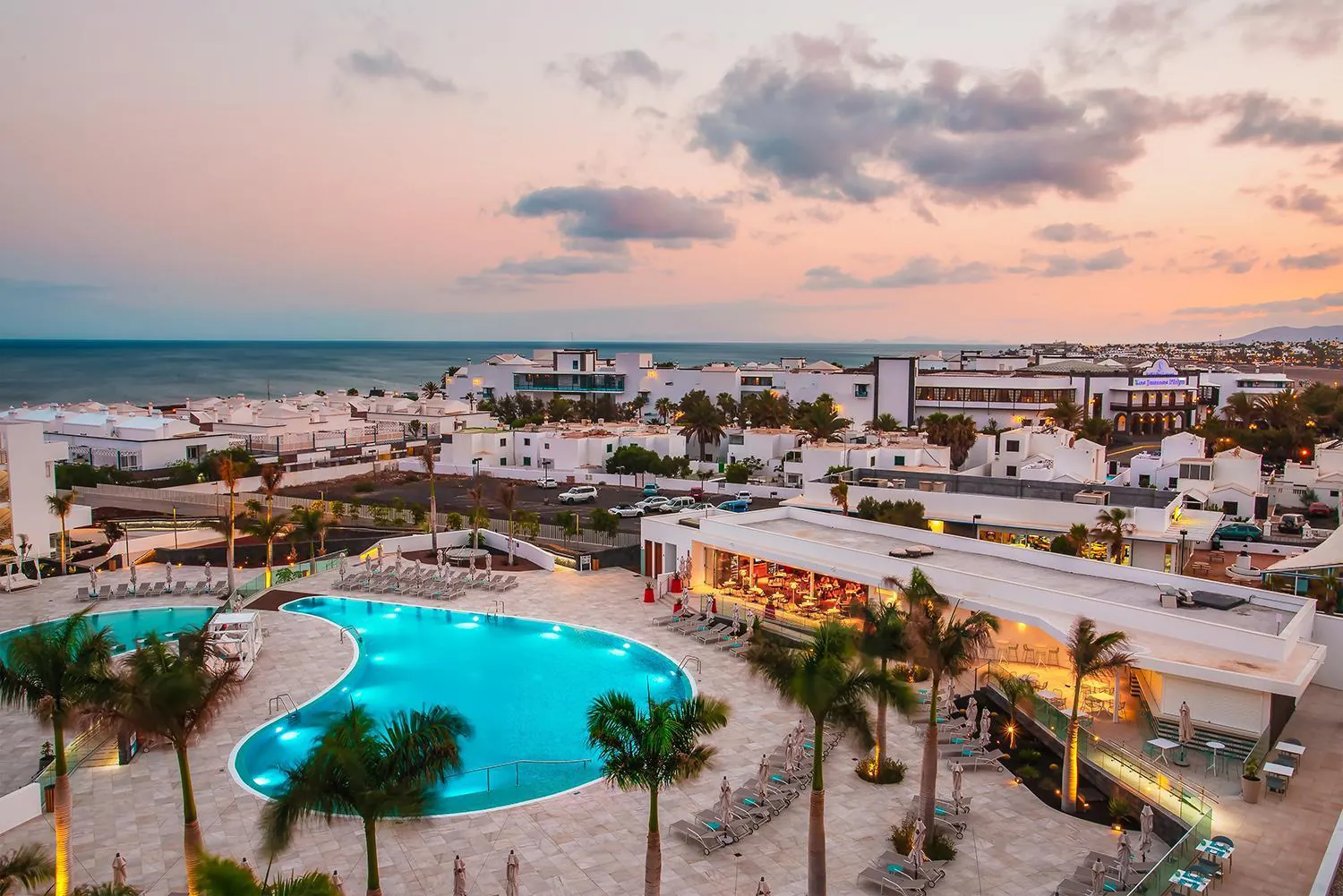 Pool terrace at dusk with the hotel and Puerto del Carmen under a pink sky