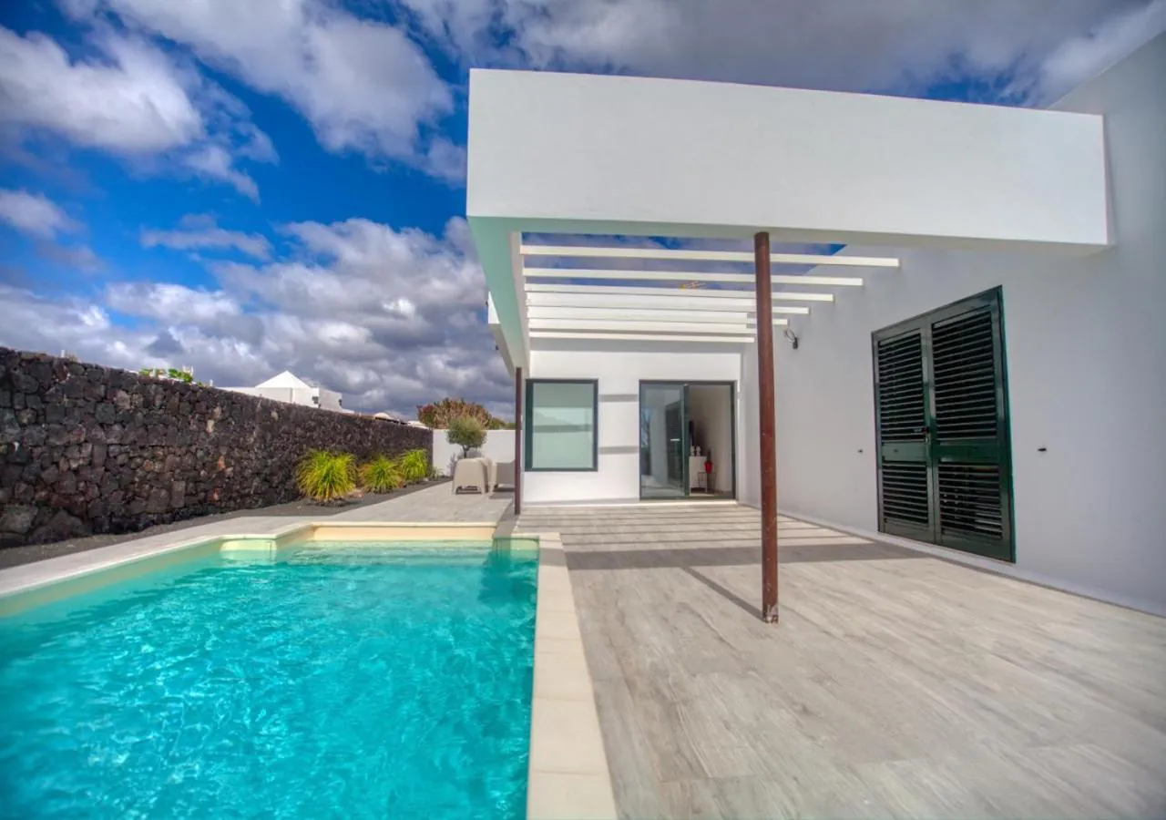 Private turquoise pool beside the villa's white terrace and pergola, volcanic stone wall behind