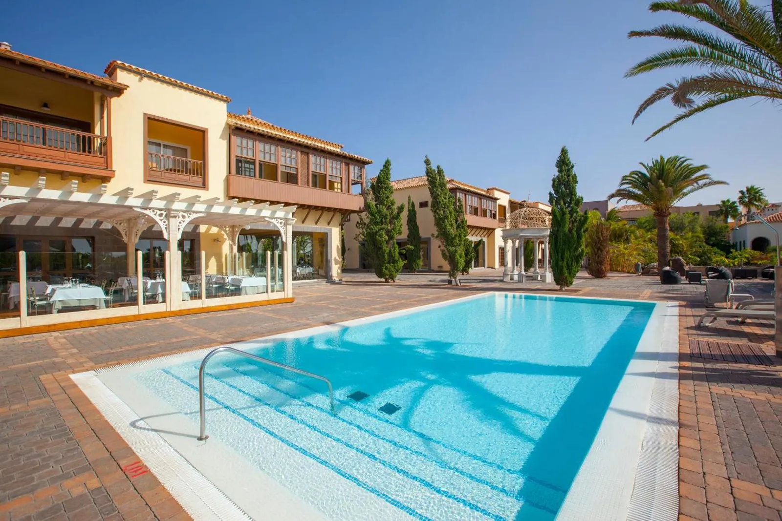 Rectangular pool lined with loungers beside the low ochre buildings