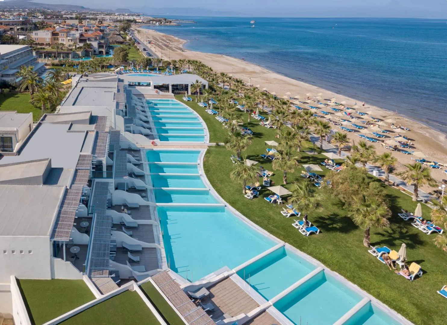 Ground-floor rooms with private pools lined up along the seafront lawn