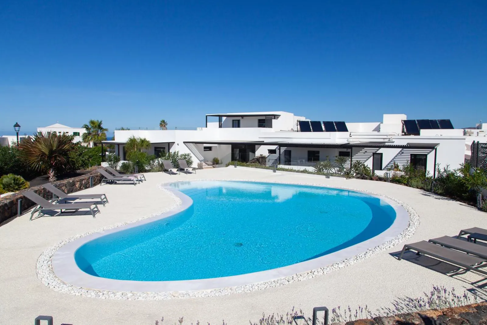 Curved outdoor pool on a pale terrace in front of Mana EcoRetreat's white low-rise buildings