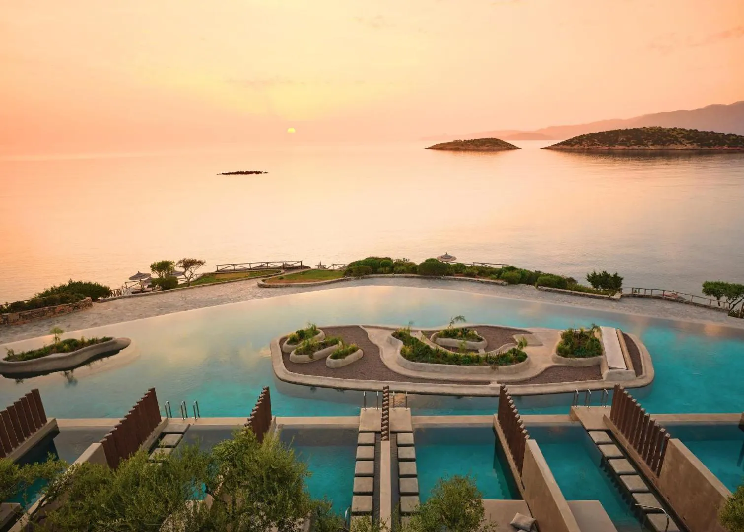 Lagoon pool on the headland at sunset, with the bay and mountains beyond