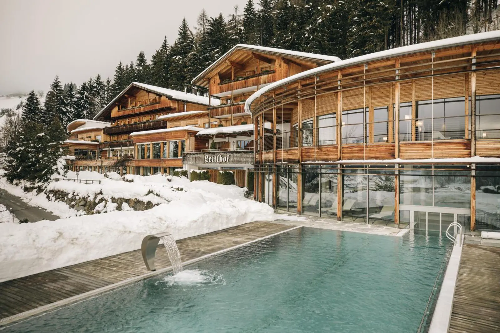 The heated outdoor pool steaming in front of the snow-covered spa building at Naturhotel Leitlhof
