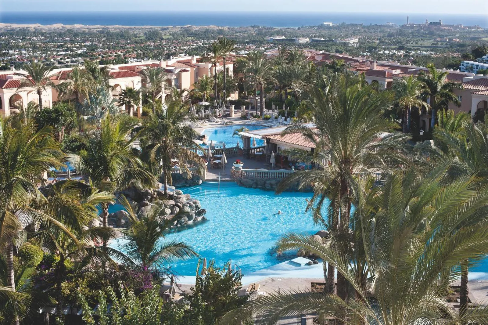 Palm Oasis Maspalomas from above: the main pool winding through palm gardens, with the coast on the horizon
