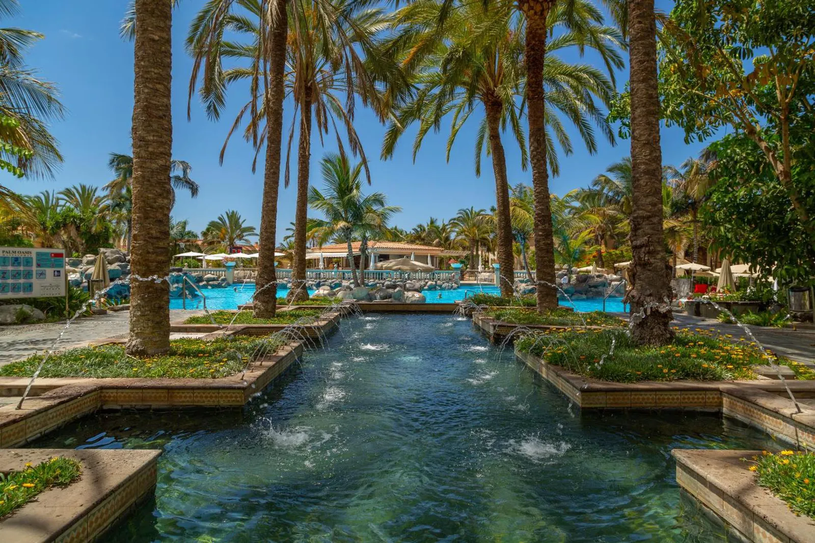 Palm-lined water channel with fountains leading towards the pools