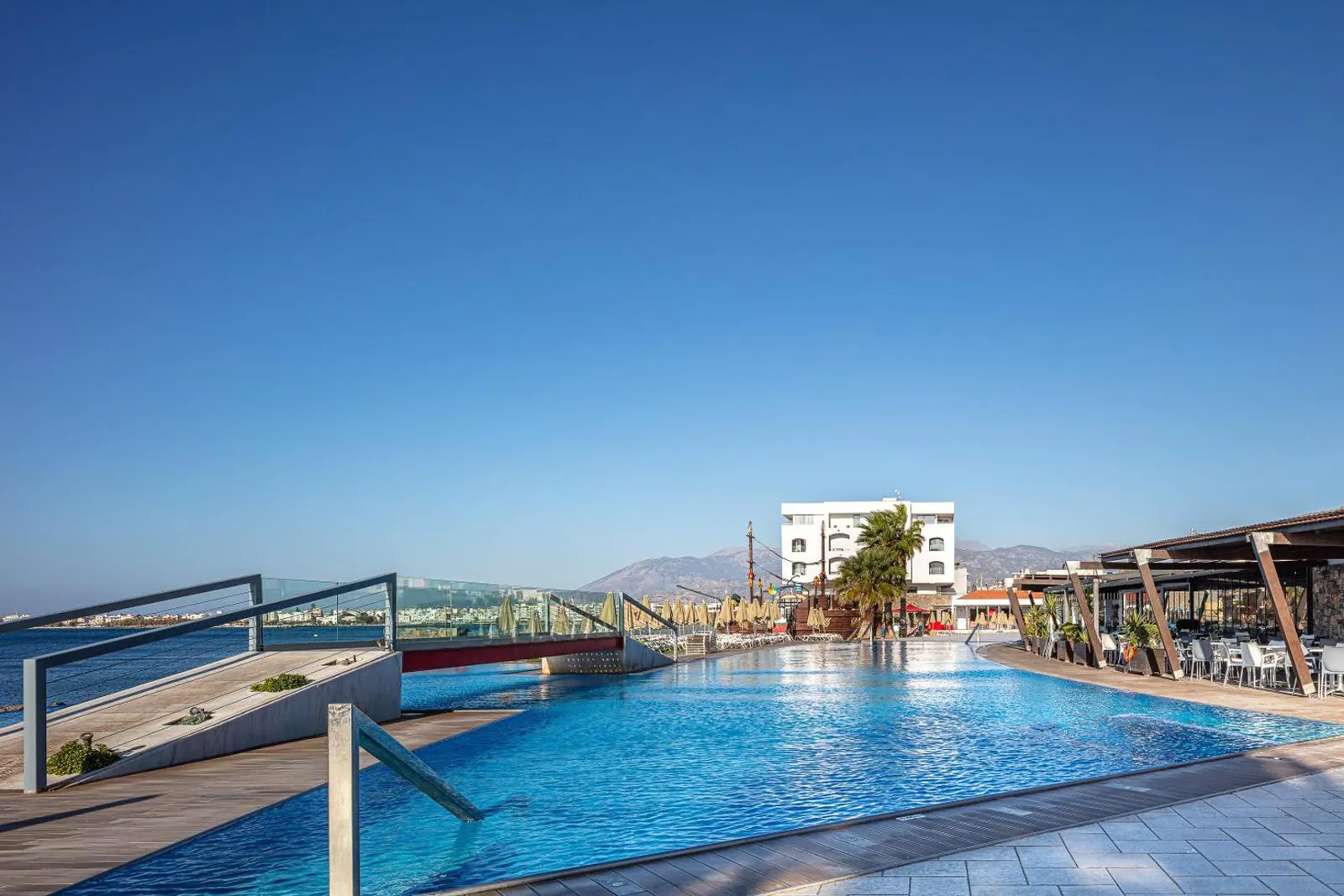 Outdoor pool along the seafront at Petra Mare, with the hotel and the mountains behind