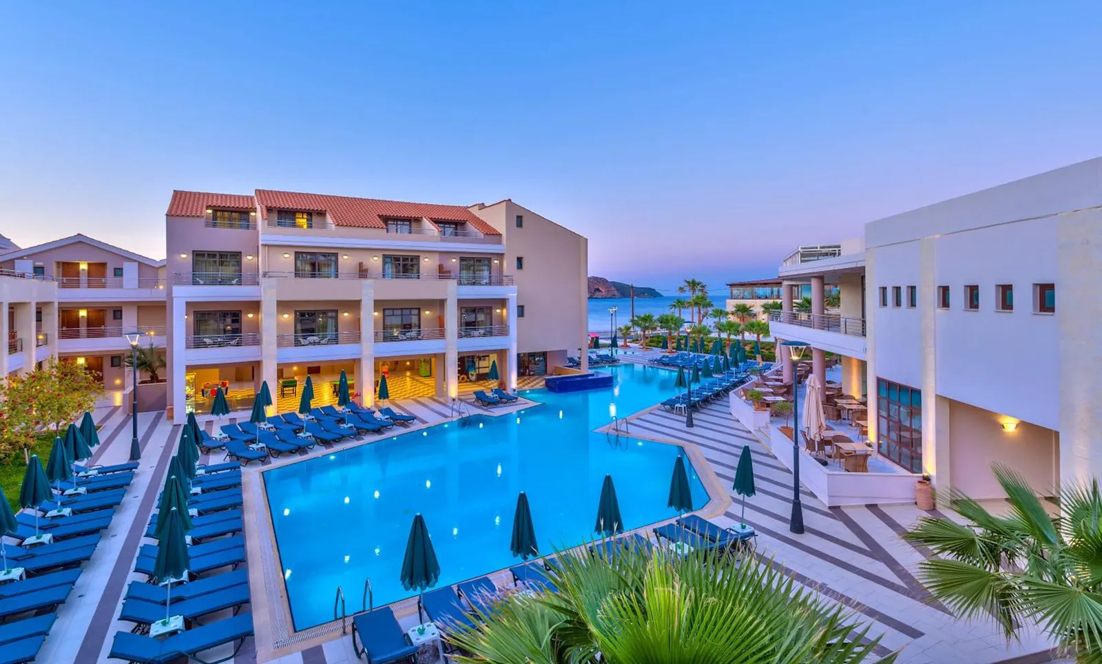 Main outdoor pool at Porto Platanias at dusk, with sunbeds along the edge and the sea behind