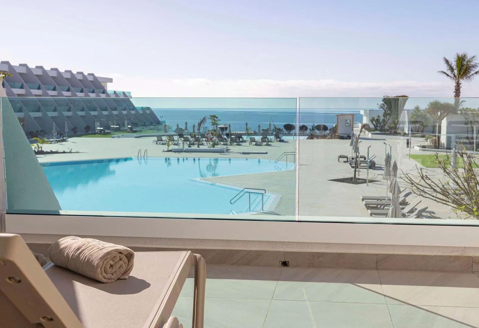 Pool terrace with loungers and the sea beyond the glass balustrade