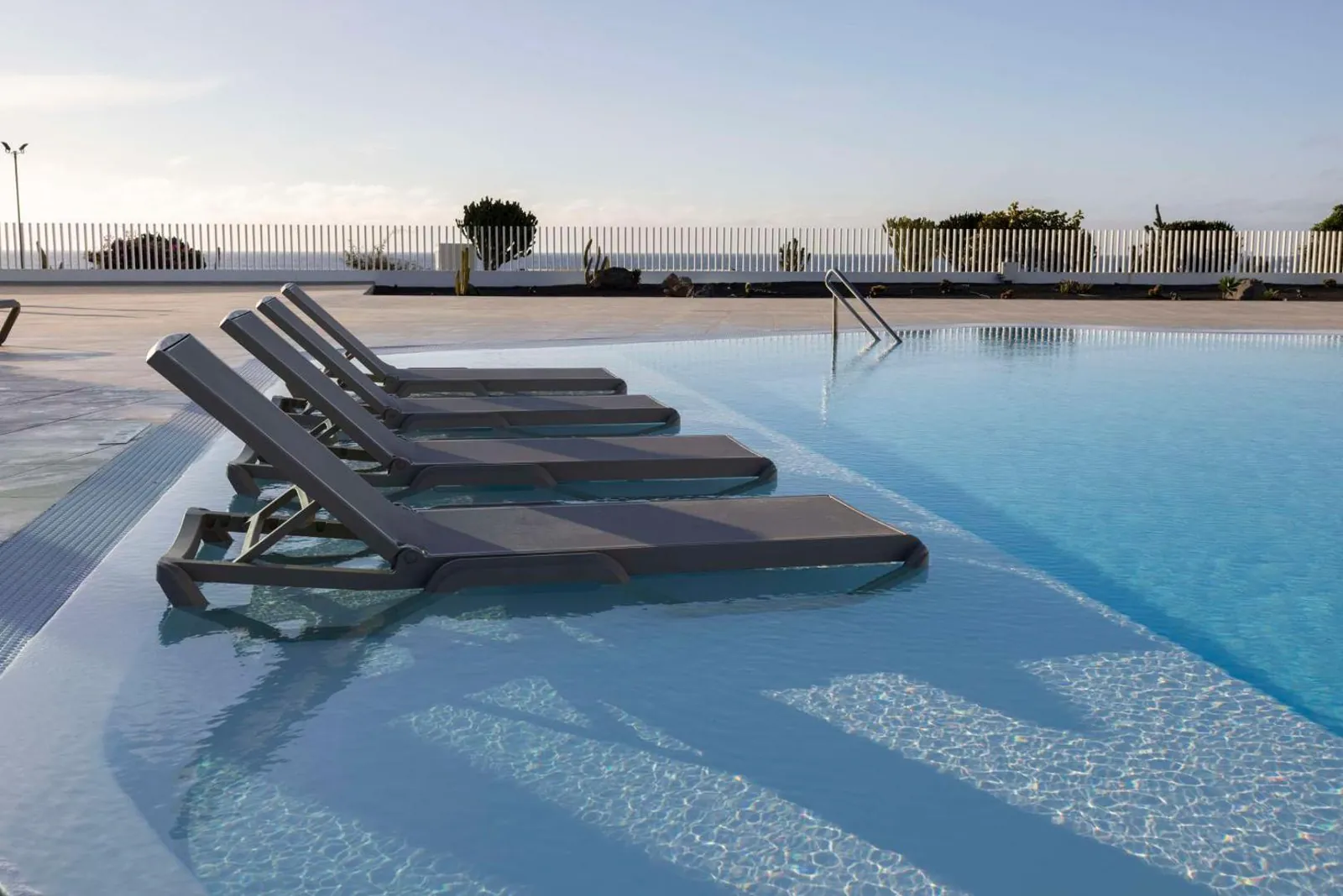 Loungers set in the shallow ledge of the pool with the ocean behind
