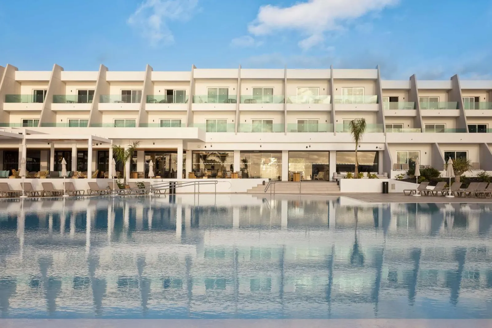 Long pool reflecting the white low-rise front of the resort