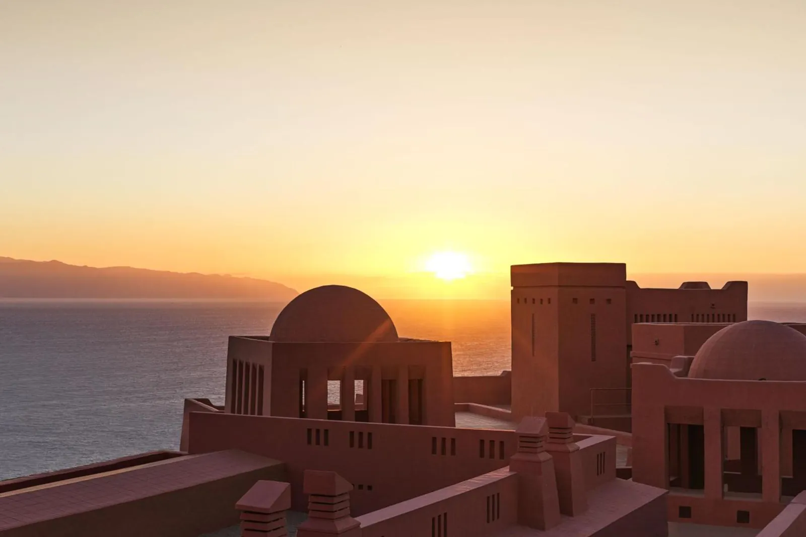 Sun setting behind a domed tower and the island of La Gomera