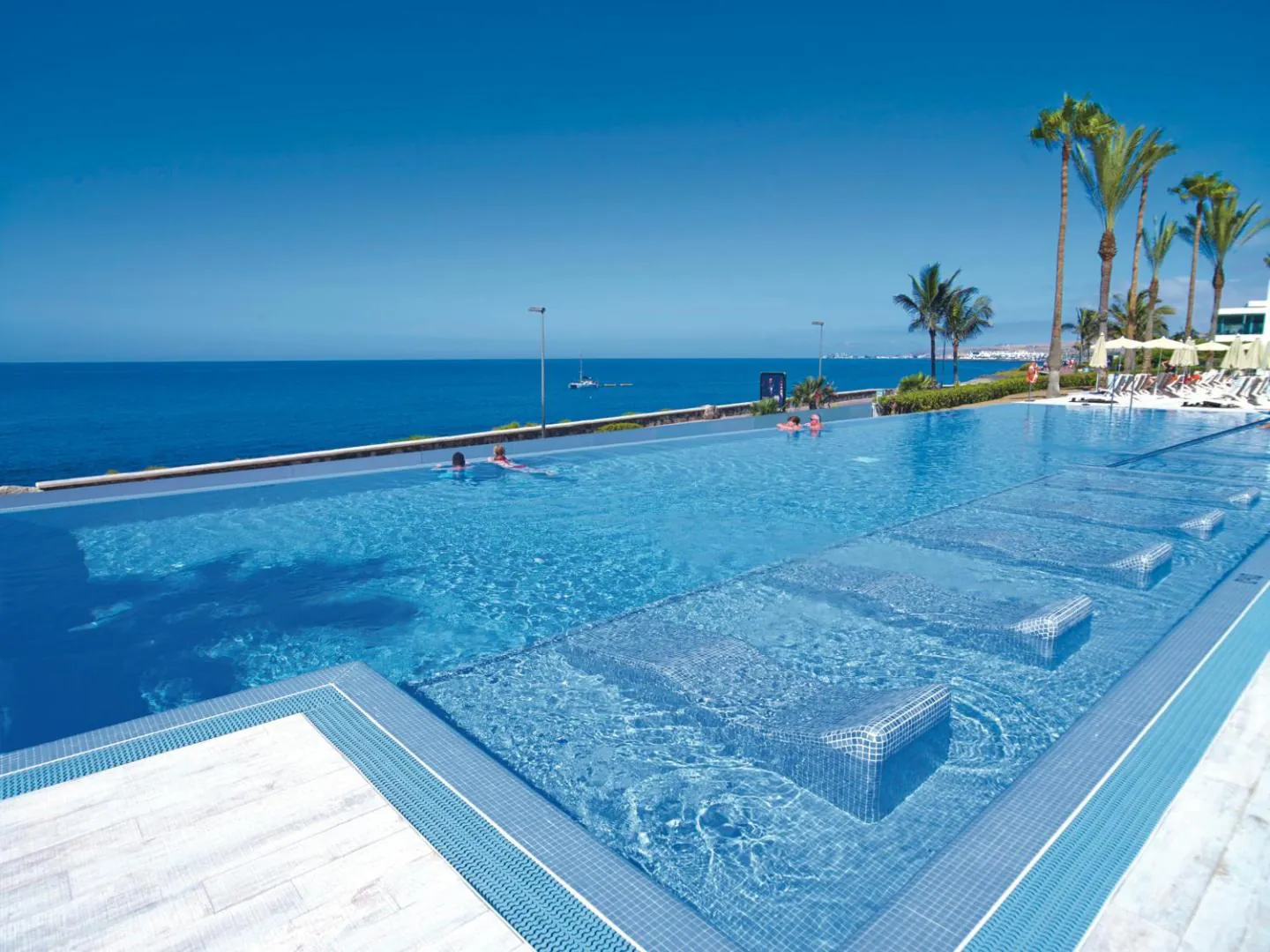 Infinity pool with submerged loungers running out towards the Atlantic at Riu Palace Meloneras