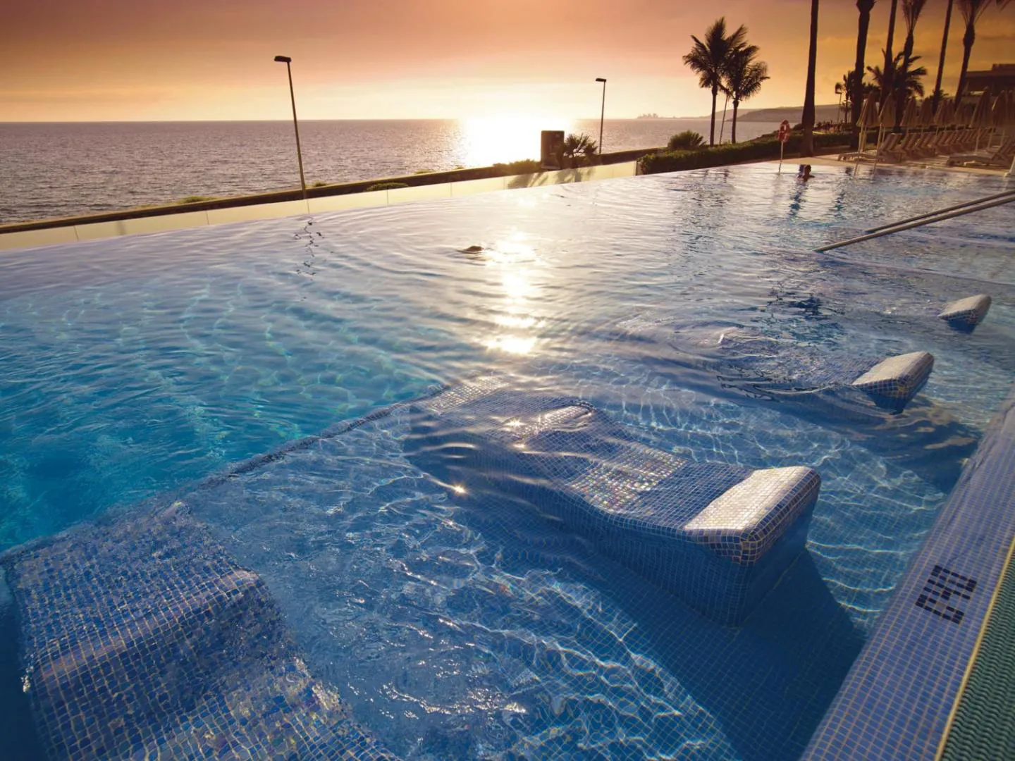 Infinity pool edge at sunset, with the sun low over the sea