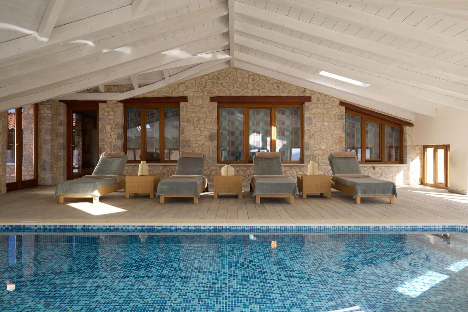 Indoor pool with loungers and stone-framed windows at Santa Marina Arachova Resort & Spa