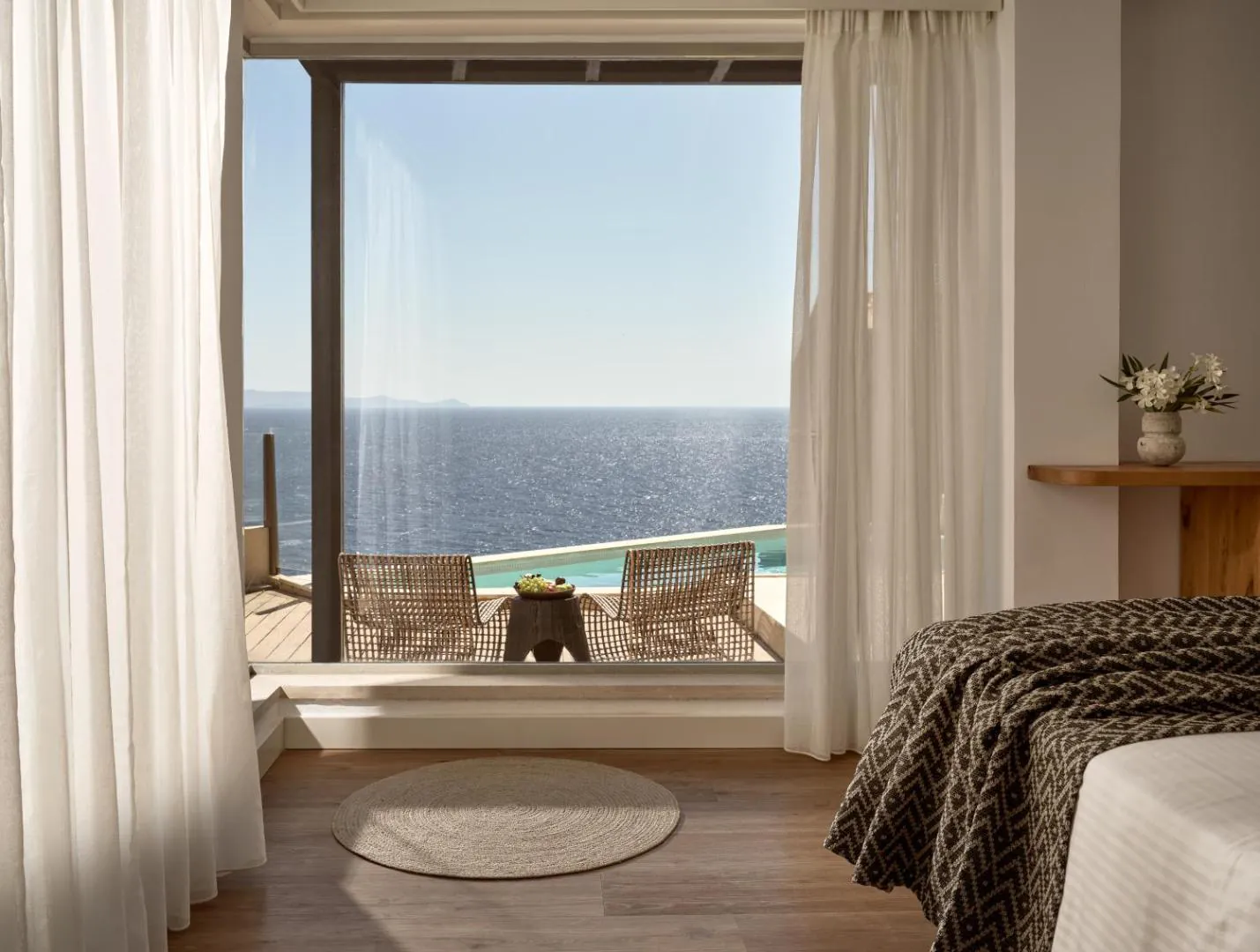 Guest room opening onto a terrace with a pool and the sea beyond