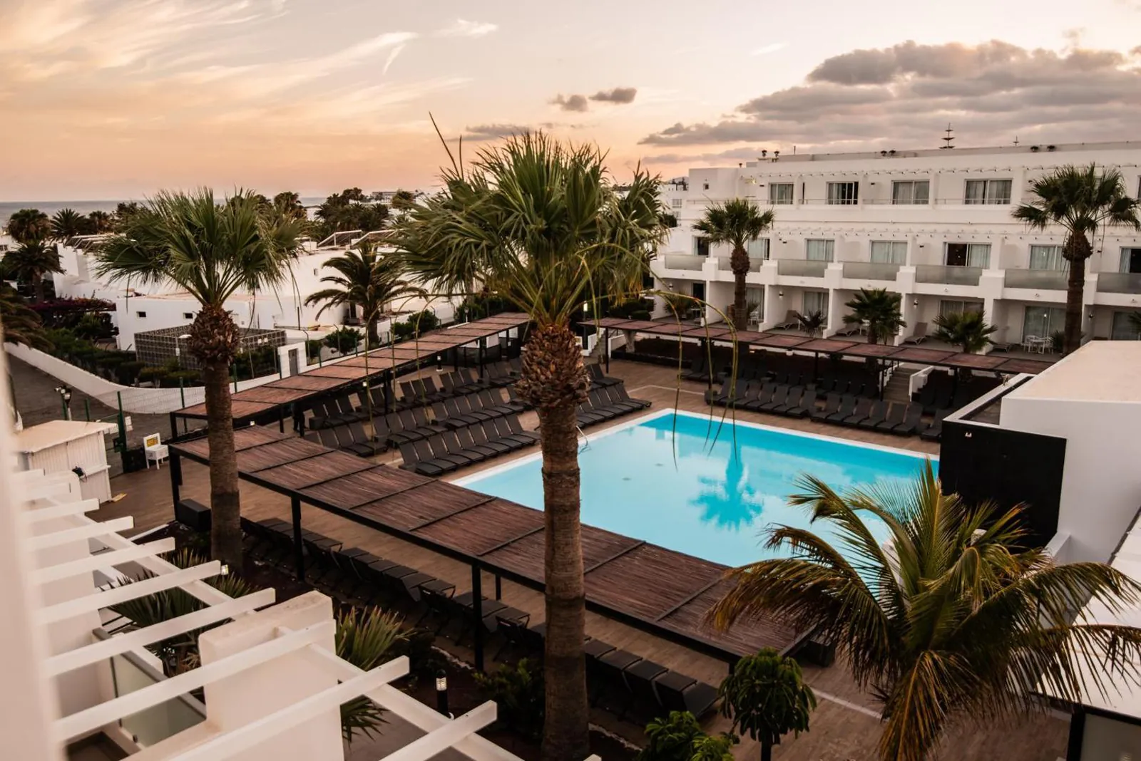 Pool courtyard framed by palms and white blocks at dusk, seen from above