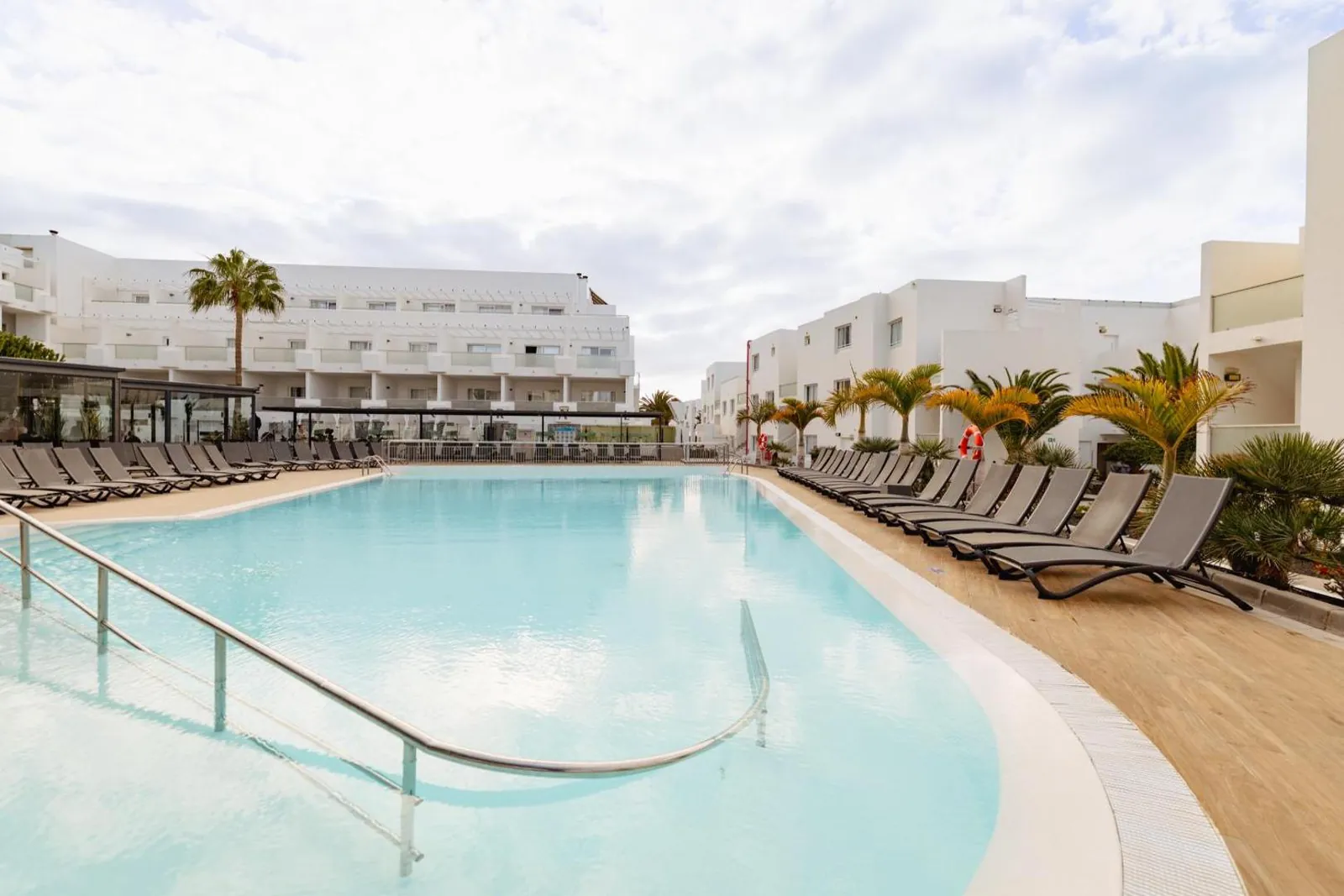 Wide lagoon-shaped pool with a gentle entry between the white buildings