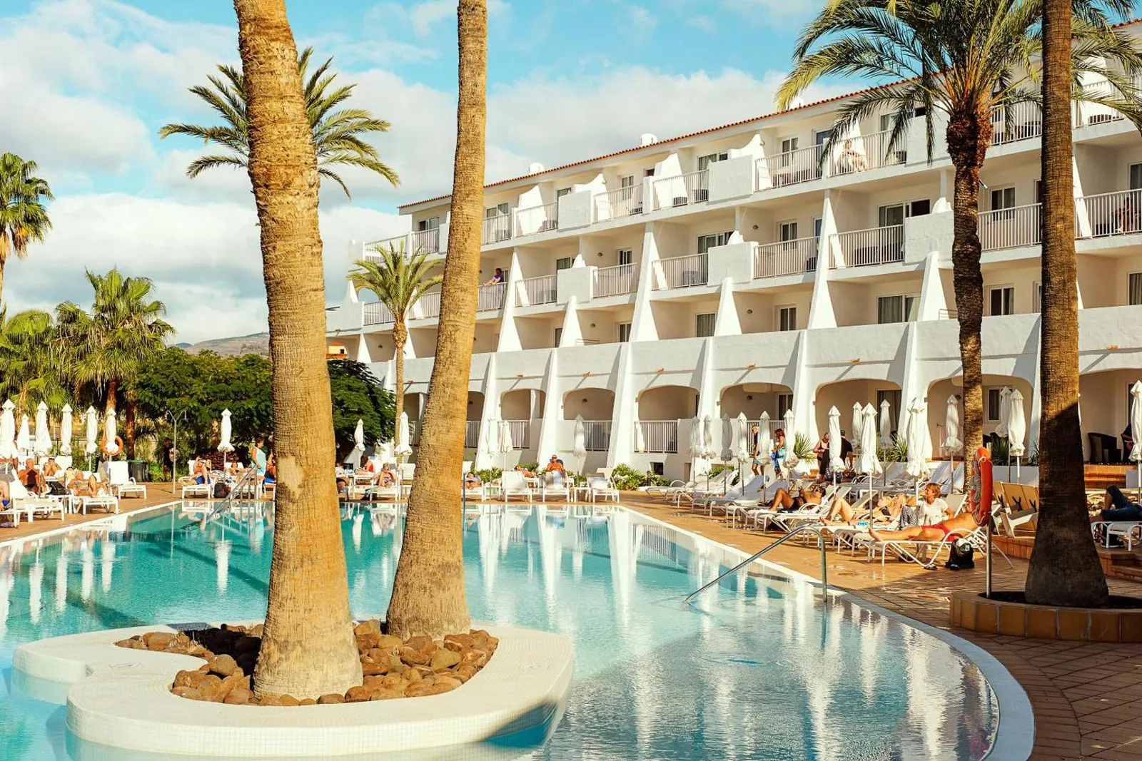 Curved pool around a palm island in front of the white suite blocks