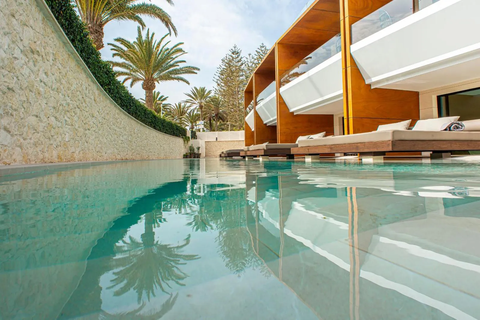 The pool curving between a stone wall and the suites' daybeds, under tall palms