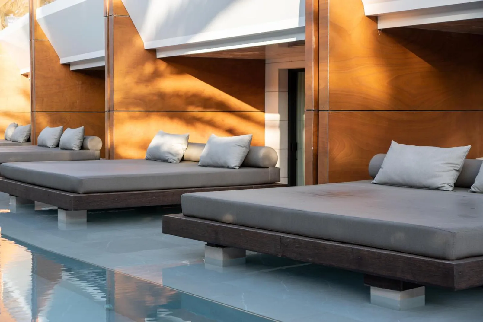 Grey daybeds set right at the edge of the pool outside the suites