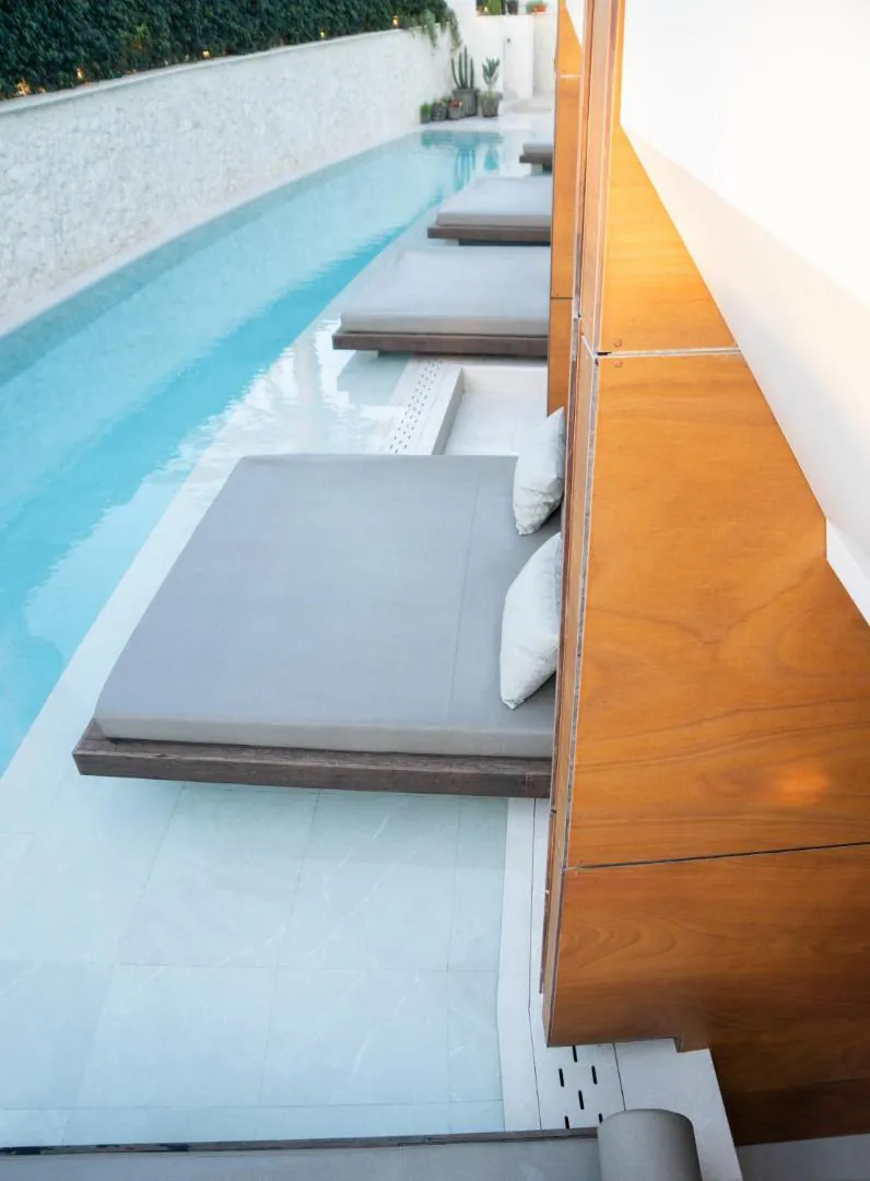 Pool-level view along the line of daybeds beside the timber-clad suites